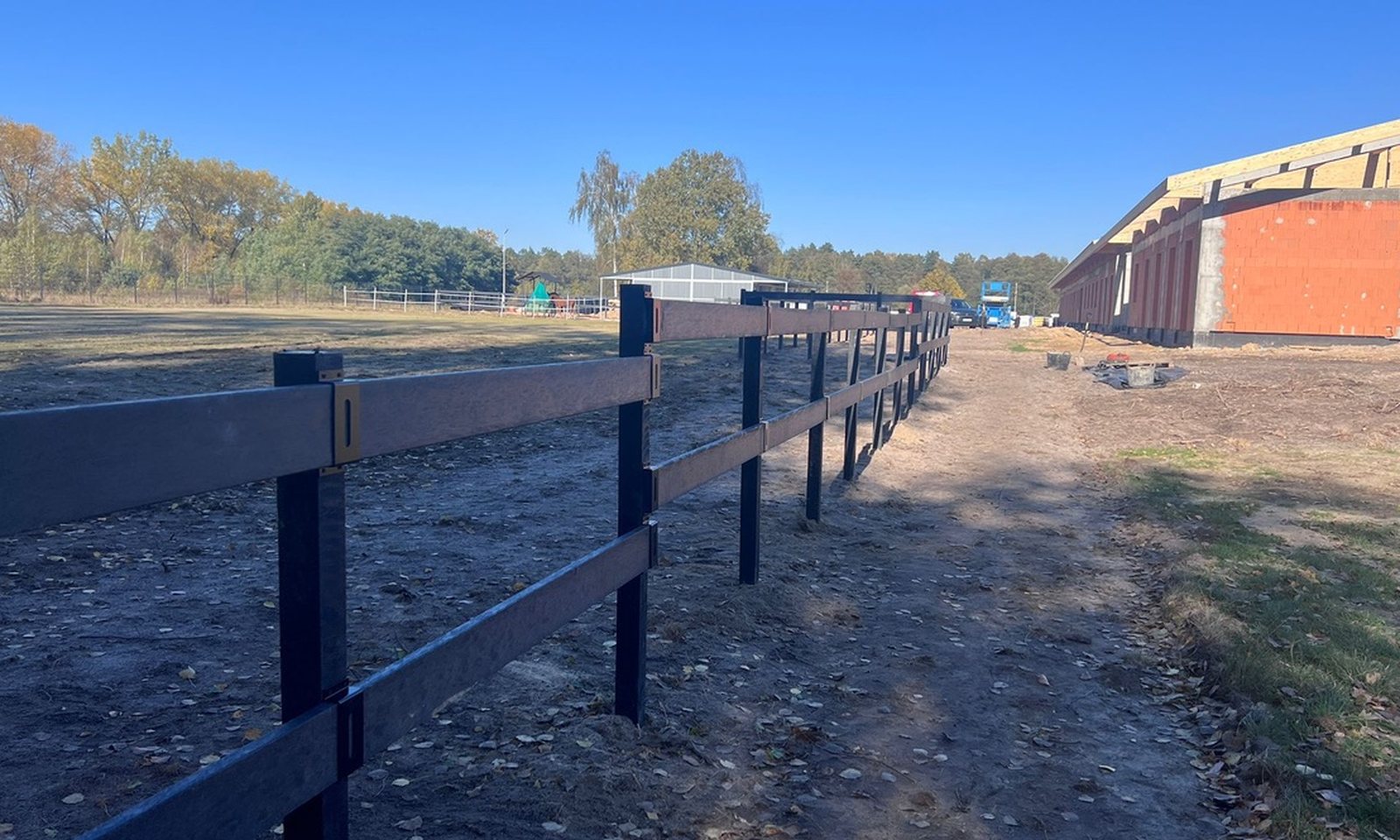 Ciąg słupków i poprzeczek EcoFarm wzdłuż budowanej hali jeździeckiej